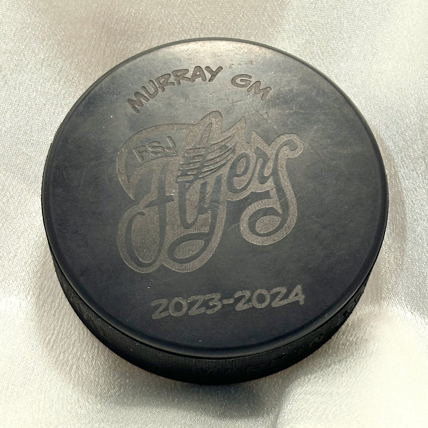 engraved hockey puck sample with Murray GM FSJ Flyers logo and the text 2023-2024 engraved below.