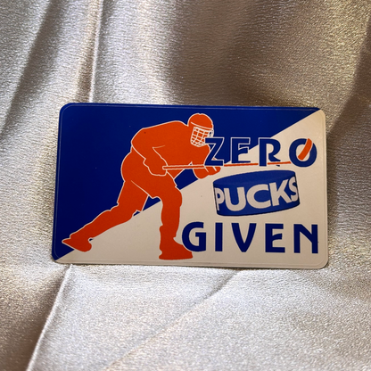 A sticker with blue and white background and orange silhouette of a hockey player with stick raised post-shot. Text on the sticker reads Zero Pucks Given.